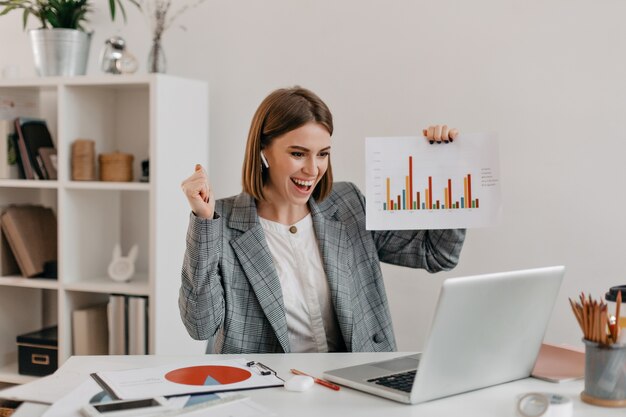 Close-up portrait of happy business woman in stylish outfit. Girl in high spirits demonstrates chart via Skype.