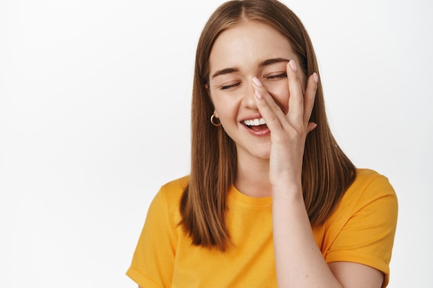 Close up portrait of happy candid girl, smiling and laughing, touching facial skin with hand, concept of skin care and cosmetic treatment advertising, white background