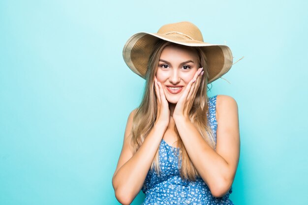 Close up portrait of a happy excited young woman in beach hat with mouth open looking at camera isolated over blue background