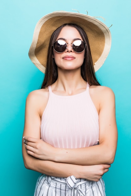 Chiuda sul ritratto di una giovane donna eccitata felice in cappello della spiaggia con la bocca aperta che guarda l'obbiettivo isolato sopra la parete blu.