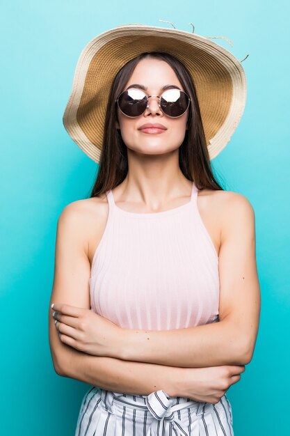 Close up portrait of a happy excited young woman in beach hat with mouth open looking at camera isolated over blue wall.