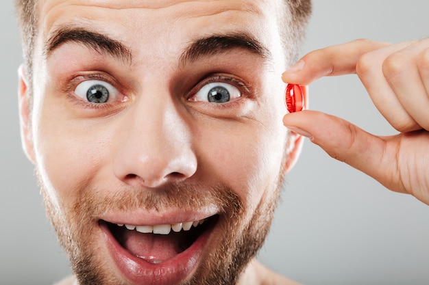 close up portrait of a happy man holding red capsule