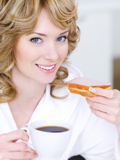 Close-up portrait of happy smiling beautiful woman eaitng sandwich and drinking coffee