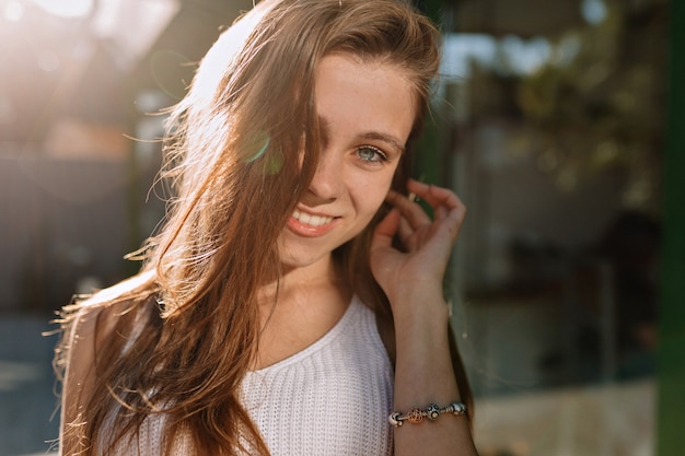 긴 머리와 파란 눈 햇빛에 카메라에 포즈를 취하는 행복 웃는 소녀의 초상화를 닫습니다