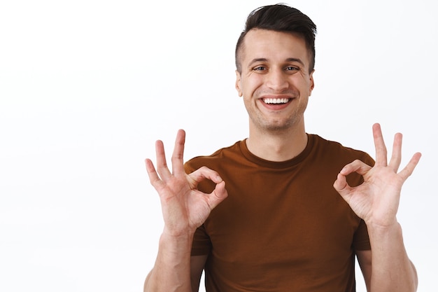 Close-up portrait of happy, smiling satisfied male customer, guy showing okay signs in approval, agree or like good quality service provided by company, recommend product, white wall