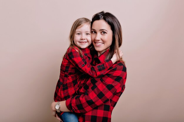 Close-up portrait of happy woman with little adorable girl wearing similar checked shirts smile and have fun, beautiful family portrait, true emotions, isolated wall, place for text