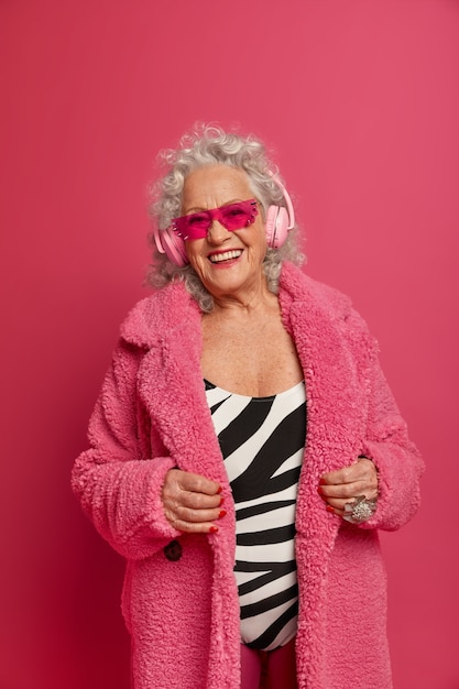 Close up portrait of happy wrinkled fashionable granny wearing pink tights and coat