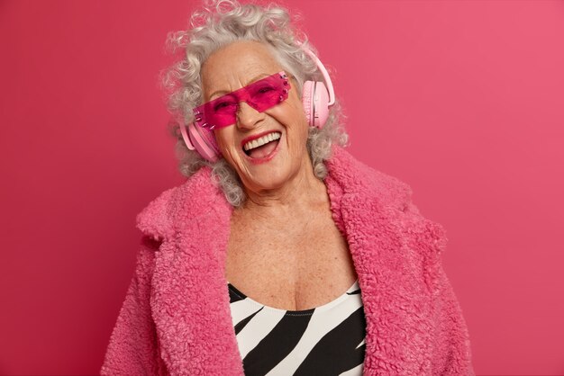 Крупным планом портрет счастливой морщинистой модной бабушки в розовых колготках и пальто