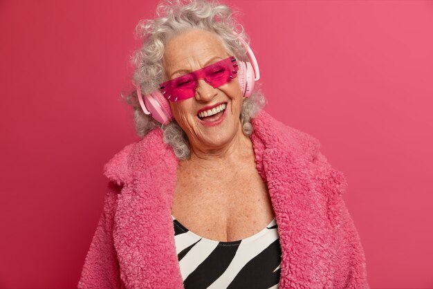 Close up portrait of happy wrinkled fashionable granny wearing pink tights and coat