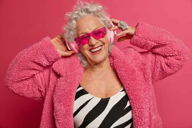 Close up portrait of happy wrinkled fashionable granny wearing pink tights and coat