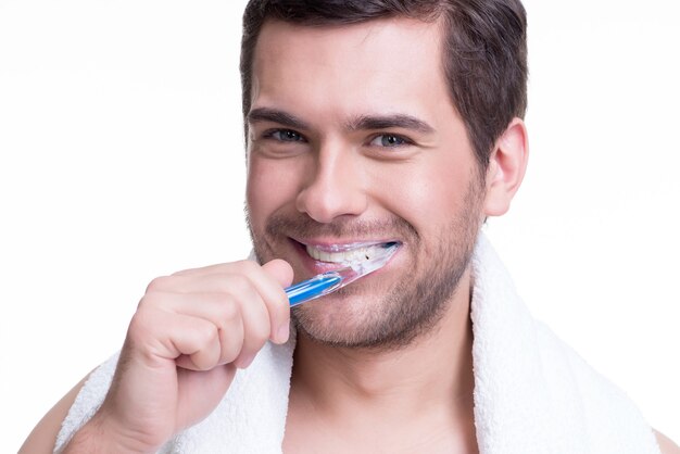 Close-up portrait of a happy young man brushing teeth on a white wall.