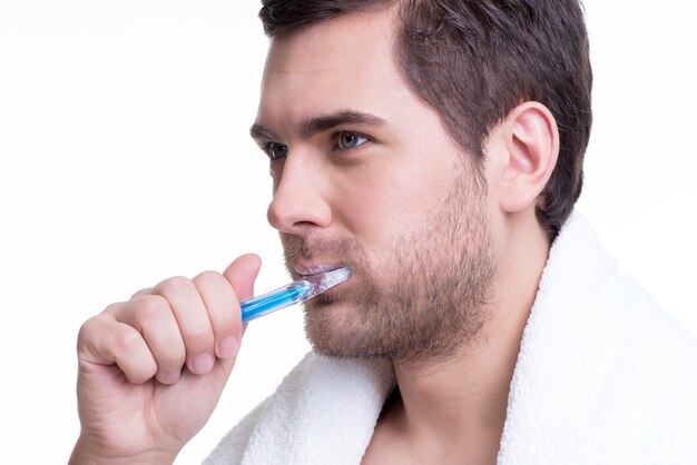 Close-up portrait of a happy young man brushing teeth on a white wall.