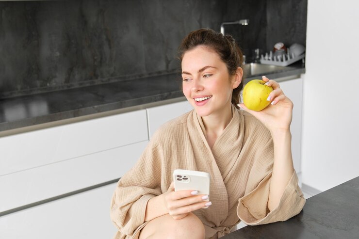 Free Photo close up portrait of happy young woman in bathrobe sitting in the kitchen and using mobile phone