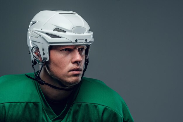 Крупным планом портрет хоккеиста в шлеме на сером фоне.
