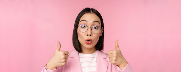 분홍색 배경을 추천하는 카메라에 놀란 표정을 하는 안경을 쓴 감동적인 기업 여성 아시아 비즈니스 여성의 초상화를 클로즈업