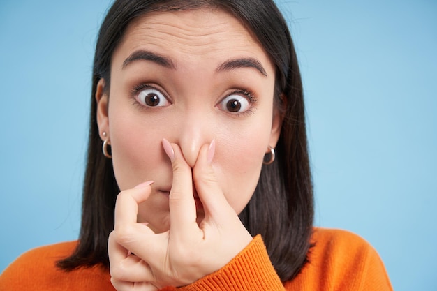 Free photo close up portrait of japanese woman shuts her nose from bad smell stands over blue background