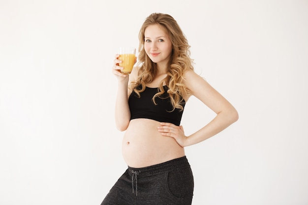 Close up portrait of joyful good-looking pregnant woman with blond hair in cozy clothes, smiling, looking in camera with happy expression