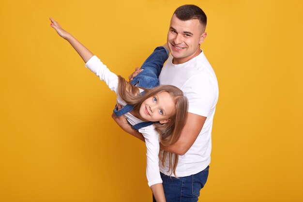 Close up portrait of kid playing with her daddy, girl being on fathers hands, pretends flying, spreads arms sideways