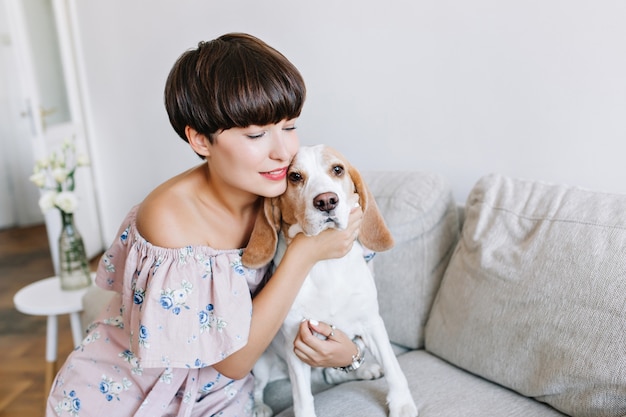 Close-up portrait of lightly tanned girl posing hugging her pet on couch