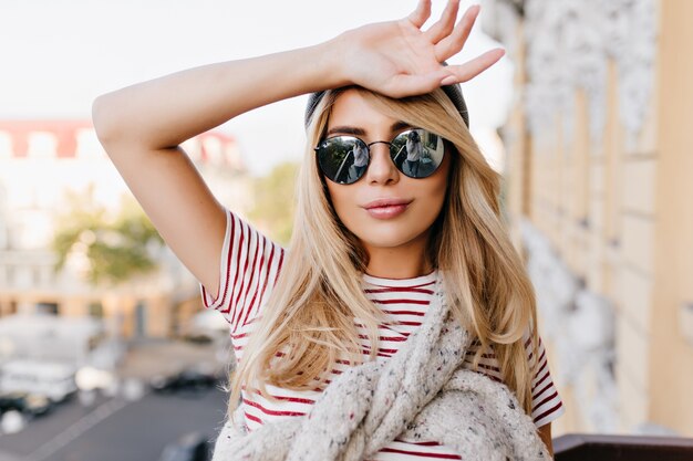 Free photo close-up portrait of lightly-tanned woman covering forehead with hand and gently smiling on blur city background