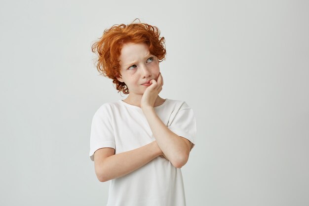 Close up portrait of little ginger boy with freckles thoughtfully looking aside remembering