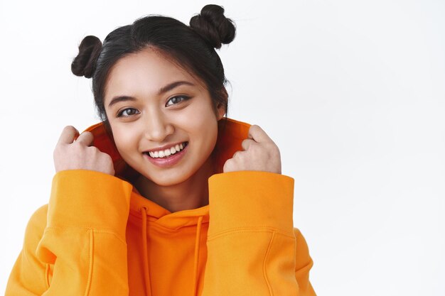 Close-up portrait of lovely and cute asian teenage girl put on hood on orange sweatshirt, smiling happy and looking camera