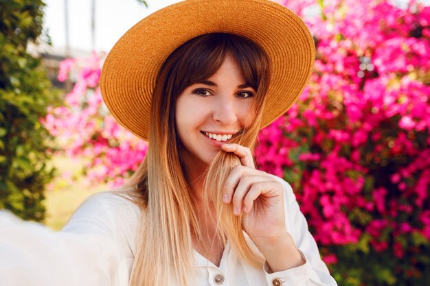 Selfieポートレートを作るトレンディな麦わら帽子の素敵な女の子の肖像画を間近します。