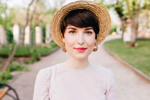Close-up portrait of lovely young lady in straw hat and cute earrings with natural nude makeup
