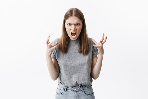 Close up portrait of mad beautiful caucasian student girl with brown hair in casual clothes  with angry face expressions, gesticulated with hands, being pissed off