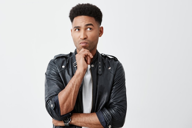 Close up portrait of mature dark-skinned man with black curly hair in casual outfit holding chin with hand, looking aside with thoughtful expression, thinking about university exams.