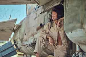 Foto gratuita ritratto ravvicinato di un meccanico in uniforme e che vola vicino, in piedi sotto un vecchio aereo bombardiere nel museo all'aperto.