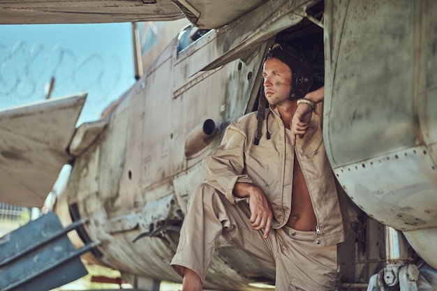 Close-up portrait of a mechanic in uniform and flying near, standing under an old bomber airplane in the open air museum.