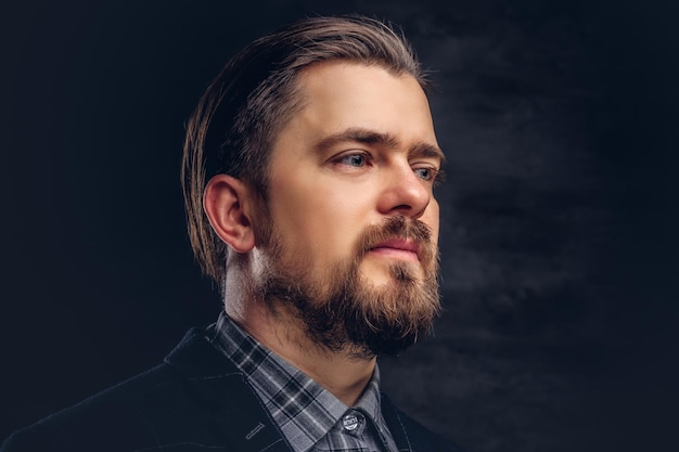 Close-up portrait of a middle-aged man with beard and hairstyle dressed in an elegant blue suit on a textured dark background in studio.