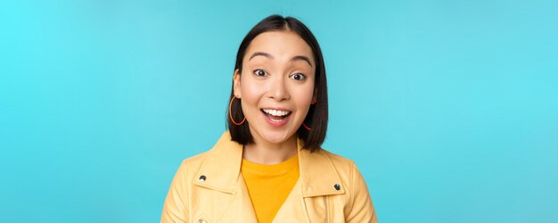 Крупный план портрета натуральной азиатской девушки, смеющейся, улыбающейся и выглядящей счастливой, стоящей над голубым фоном