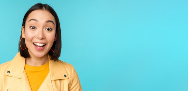 Close up portrait of natural asian girl laughing smiling and looking happy standing over blue background Copy space