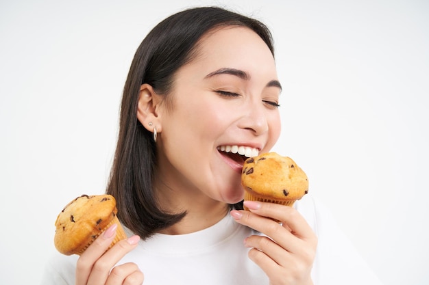 無料写真 アジアの女の子が白い背景で隔離の幸せそうな顔でカップケーキを食べるの肖像画を間近します。