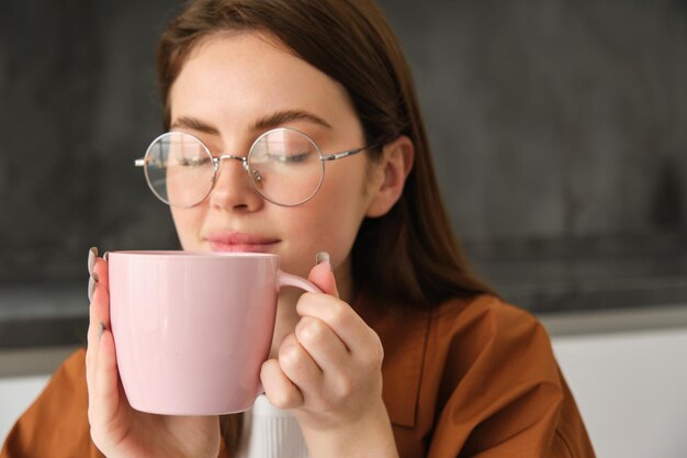 無料写真 眼鏡をかぶった美しい茶色の女性のクローズアップ肖像画 ⁇ コーヒーの ⁇ いがするカップでお茶を飲む