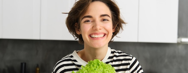 Бесплатное фото Близкий портрет красивой здоровой улыбающейся женщины, позирующей с зеленым листом салата для приготовления пищи