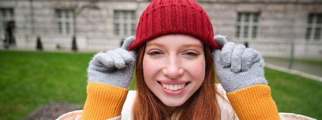 無料写真 赤いニット帽暖かい手袋を着て笑顔で探している美しい赤毛の女性の肖像画を間近します。