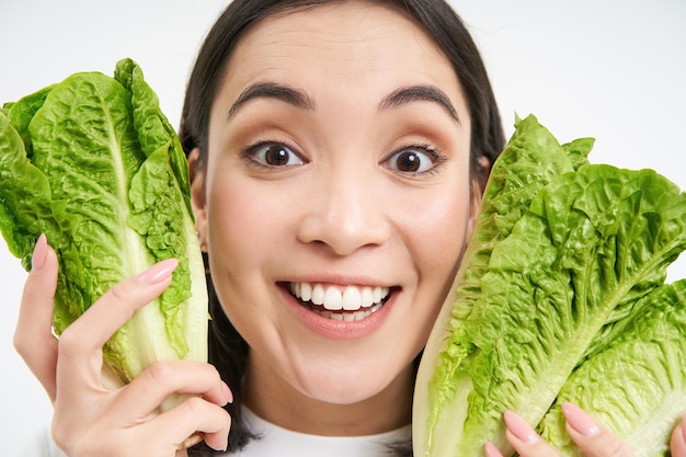 無料写真 幸せな韓国人女性のクローズ アップの肖像画は、野菜が好きなキャベツを食べるレタスで顔を示しています