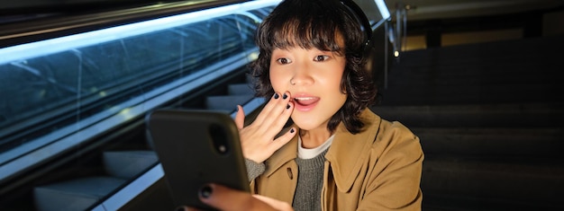 無料写真 韓国の女の子のクローズアップポートレートは、携帯電話で何か素晴らしいものを読んで驚いているように見えます
