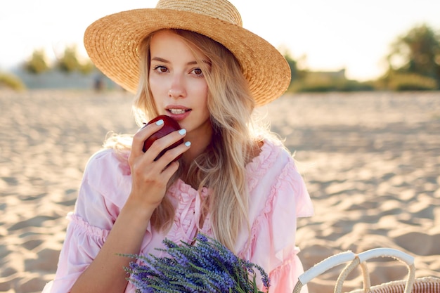 Бесплатное фото Закройте вверх по портрету естественной белой девушки в соломенной шляпе, наслаждаясь выходными около океана. позирует с фруктами. букет лаванды в соломенном мешочке.