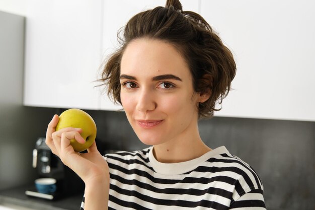 無料写真 健康的な果物を食べているリンゴを持ったキッチンで笑顔の女性の肖像画を閉じる
