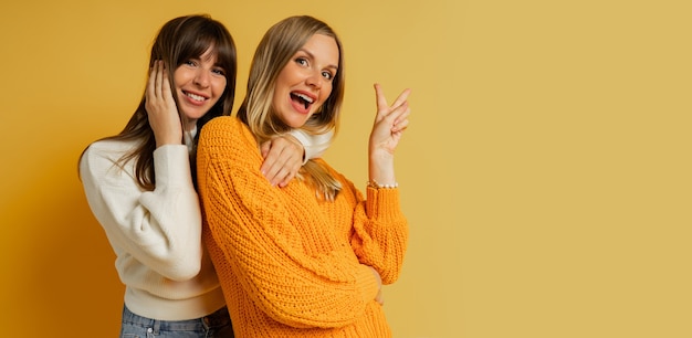 Закройте вверх по портрету двух симпатичных женщин в уютных свитерах, позирующих на желтом. осенние и зимние модные тенденции.