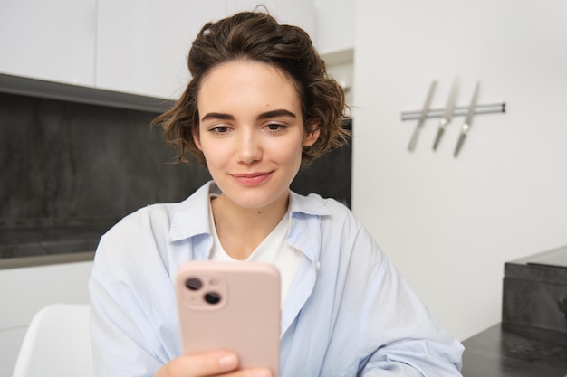 Бесплатное фото Крупный план портрета молодой брюнетки, читающей на мобильном телефоне, сидящей дома с помощью смартфона