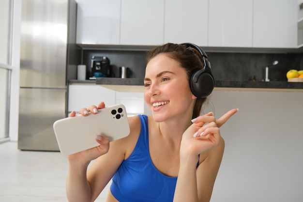 Бесплатное фото Крупный план портрета молодой счастливой женщины, тренирующейся дома, слушающей музыку в беспроводных наушниках и поющей