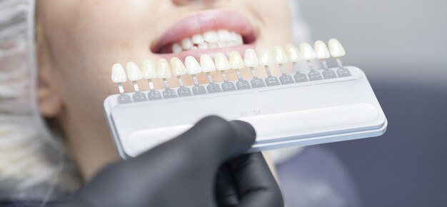 Крупным планом портрет молодой женщины в кресле стоматолога, проверьте и выберите цвет зубов. стоматолог делает процесс лечения в кабинете стоматологической клиники. стоматолог