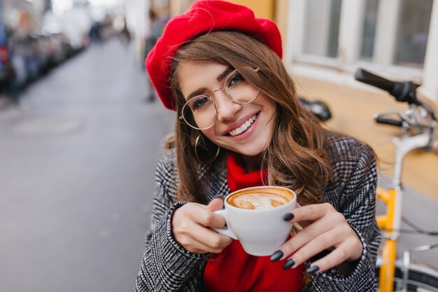 Close-up portrait of pale brunette girl with charming smile gently holding cup of coffee