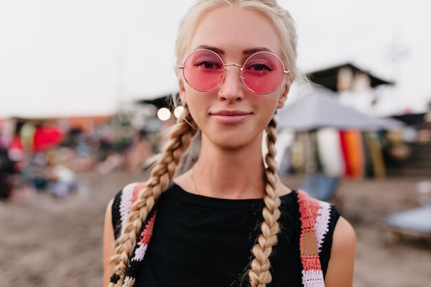 Close-up portrait of pleased fair-haired woman wears round pink sunglasses.