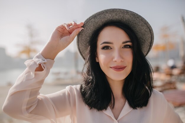 Крупным планом портрет позитивной брюнетки женщины в винтажной шляпе, позирующей на открытом воздухе